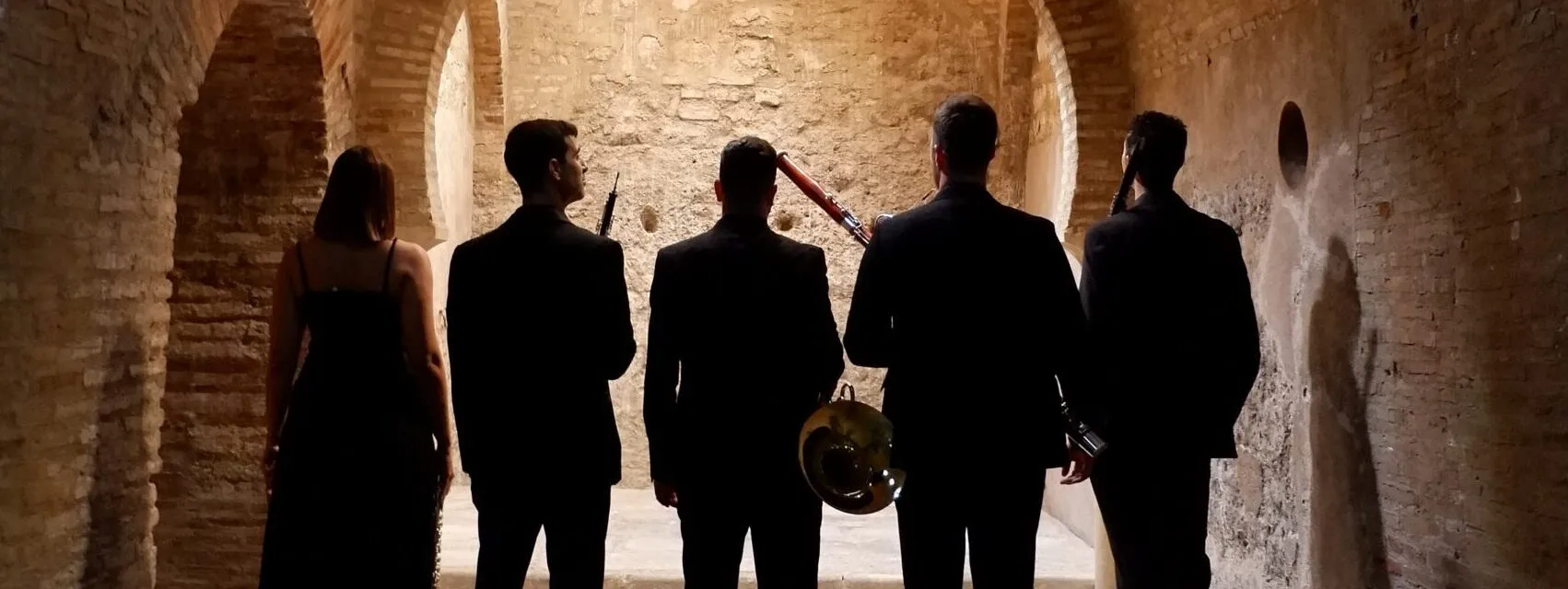 Los cinco músicos de Zayt Ensemble, de espaldas, en un patio de arcos de piedra
